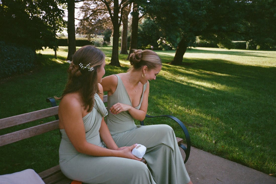 Two bridesmaids sitting together on a bench in the afternoon.